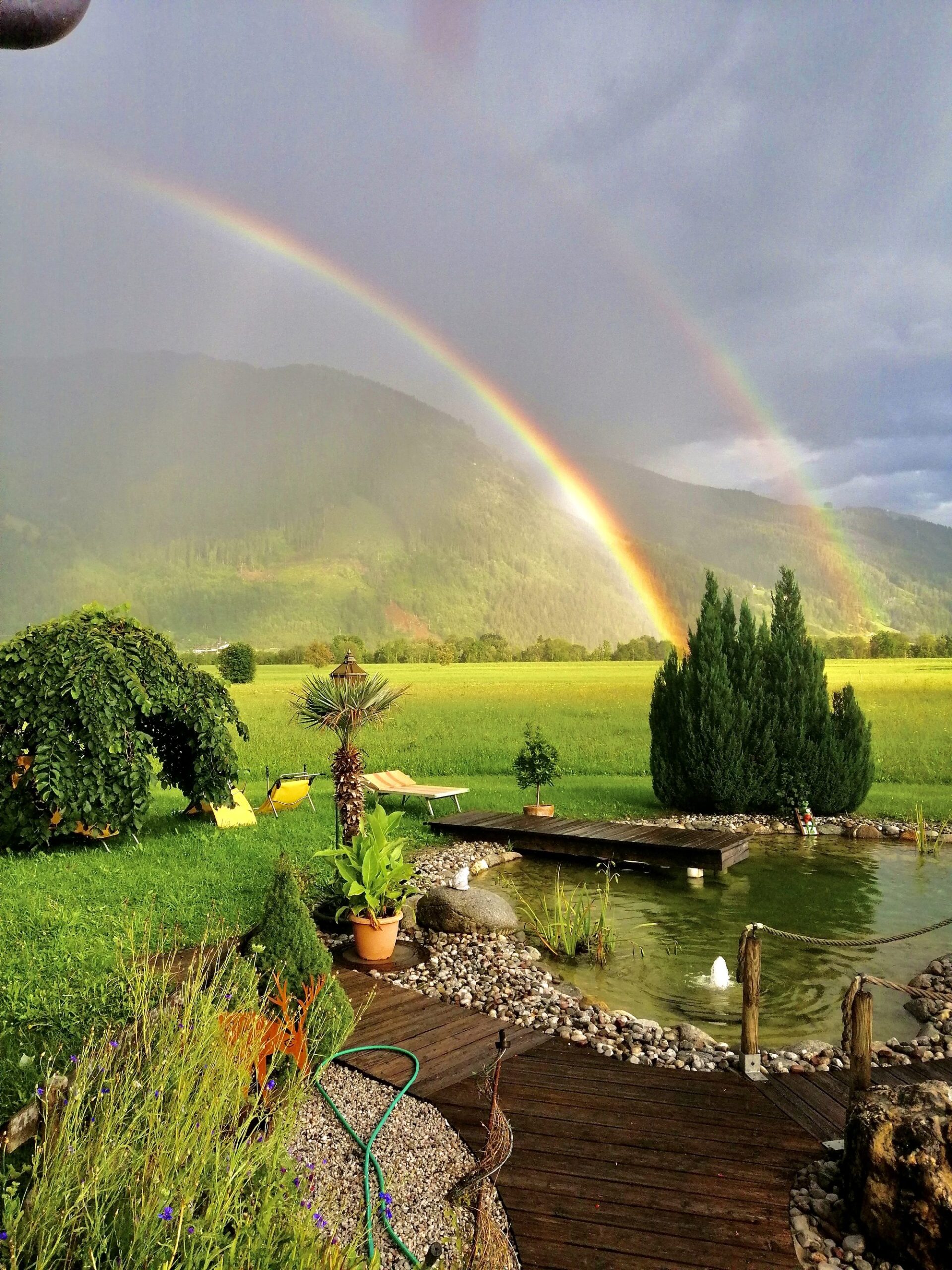 Doppelter Regenbogen über grünem Feld und Naturteich beim Landhaus Quehenberger in Maishofen