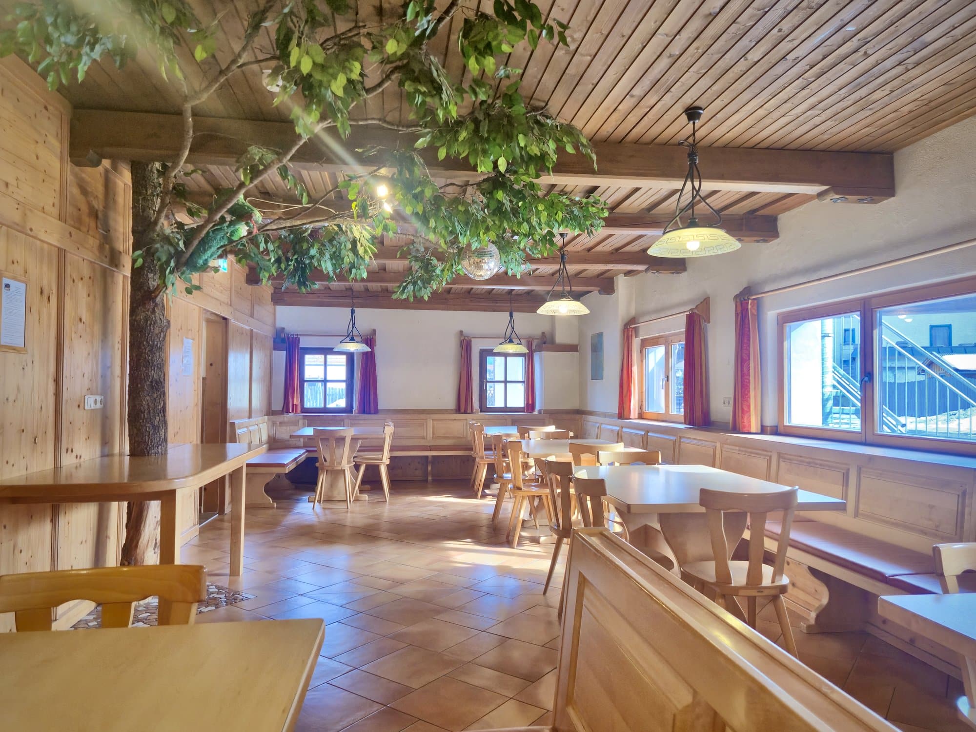 Heller Speisesaal im Selbstversorgerhaus Maishofen mit dekorativem Baum, Diskokugel und gemütlichen Holztischen.