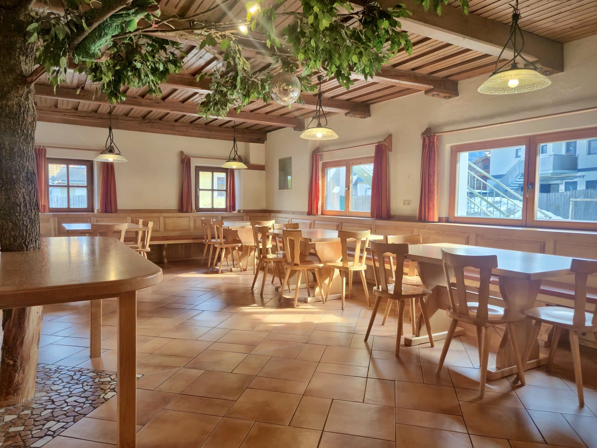 Großer Speisesaal im Selbstversorgerhaus Maishofen mit dekorativem Innenbaum und Diskokugel an der Holzdecke