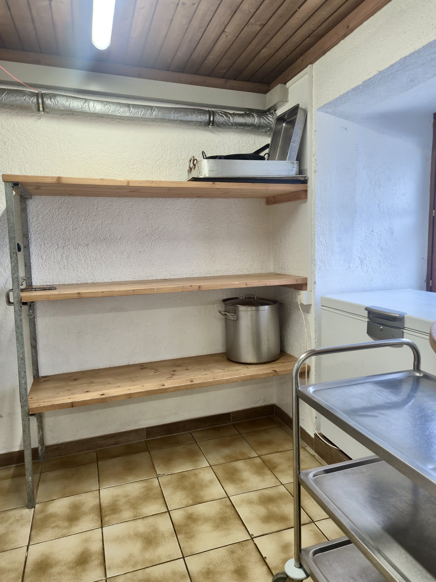Lagerraum im Selbstversorgerhaus Maishofen mit Holzregalen, großem Kochtopf und Durchgang zur Kühlzelle