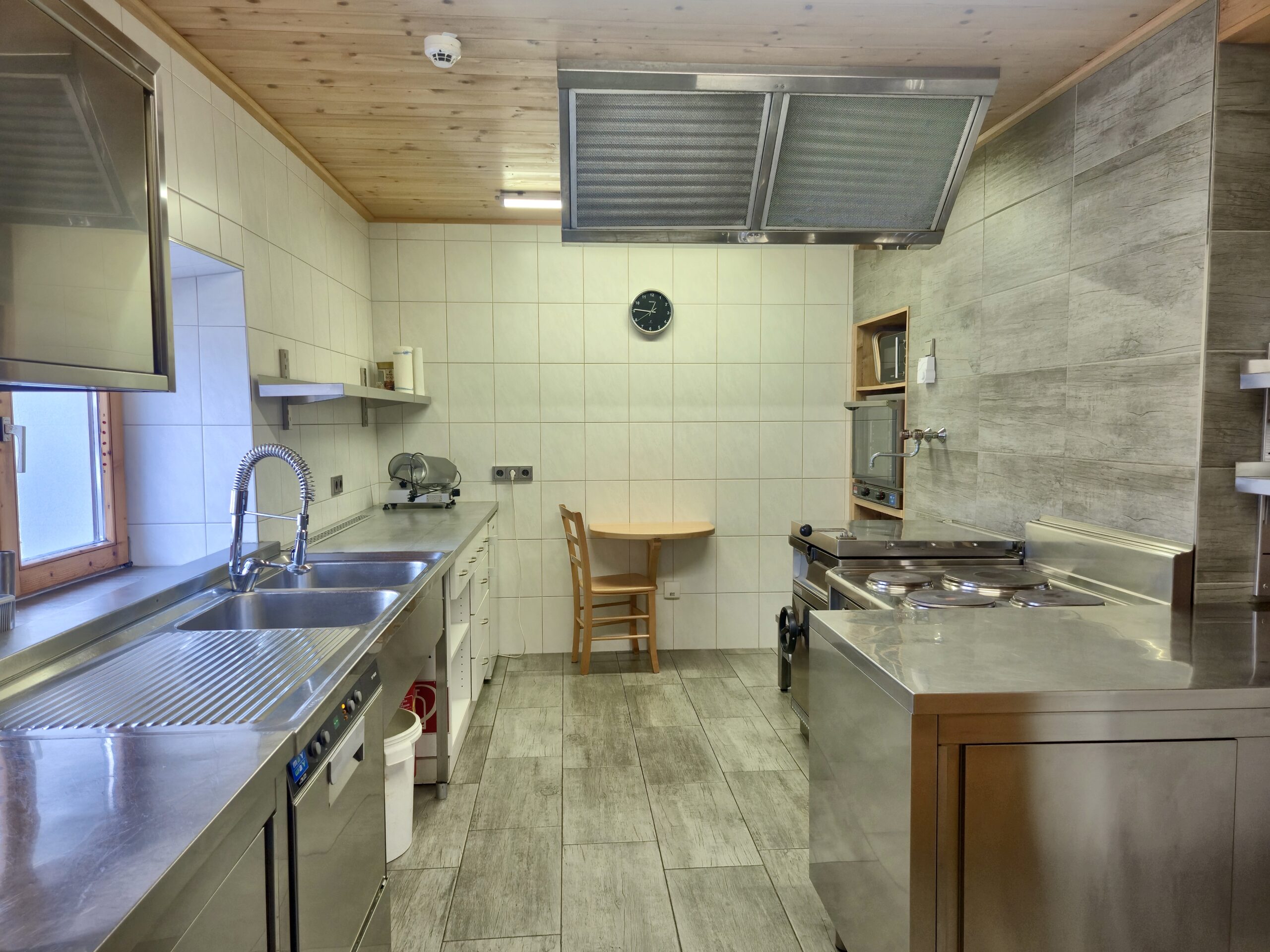 Moderne Gastro-Küche im Selbstversorgerhaus Maishofen mit Edelstahl-Arbeitsflächen und großem Dunstabzug