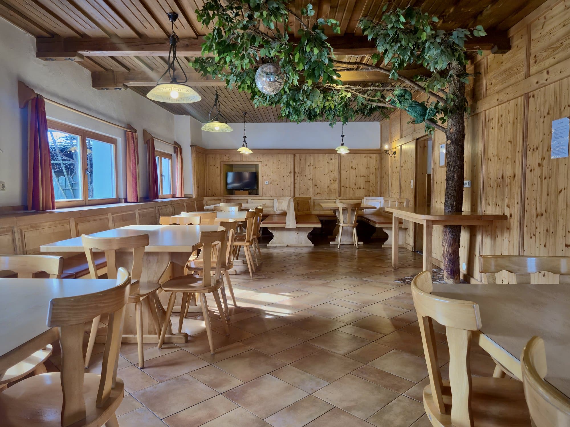 Großer Speisesaal im Selbstversorgerhaus Maishofen mit dekorativem Baum, Holzvertäfelung und Sitzmöglichkeiten für Gruppen