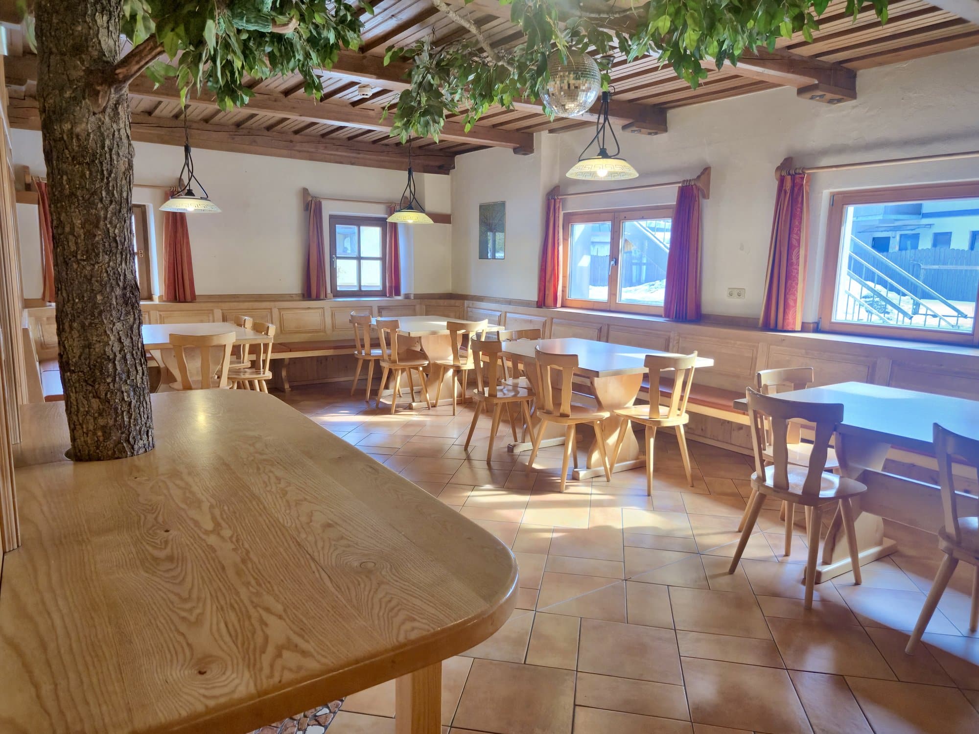 Speisesaal im Selbstversorgerhaus Maishofen mit rustikaler Holzvertäfelung, großem Baumstamm im Raum und gemütlicher Sitzgelegenheit für Gruppen