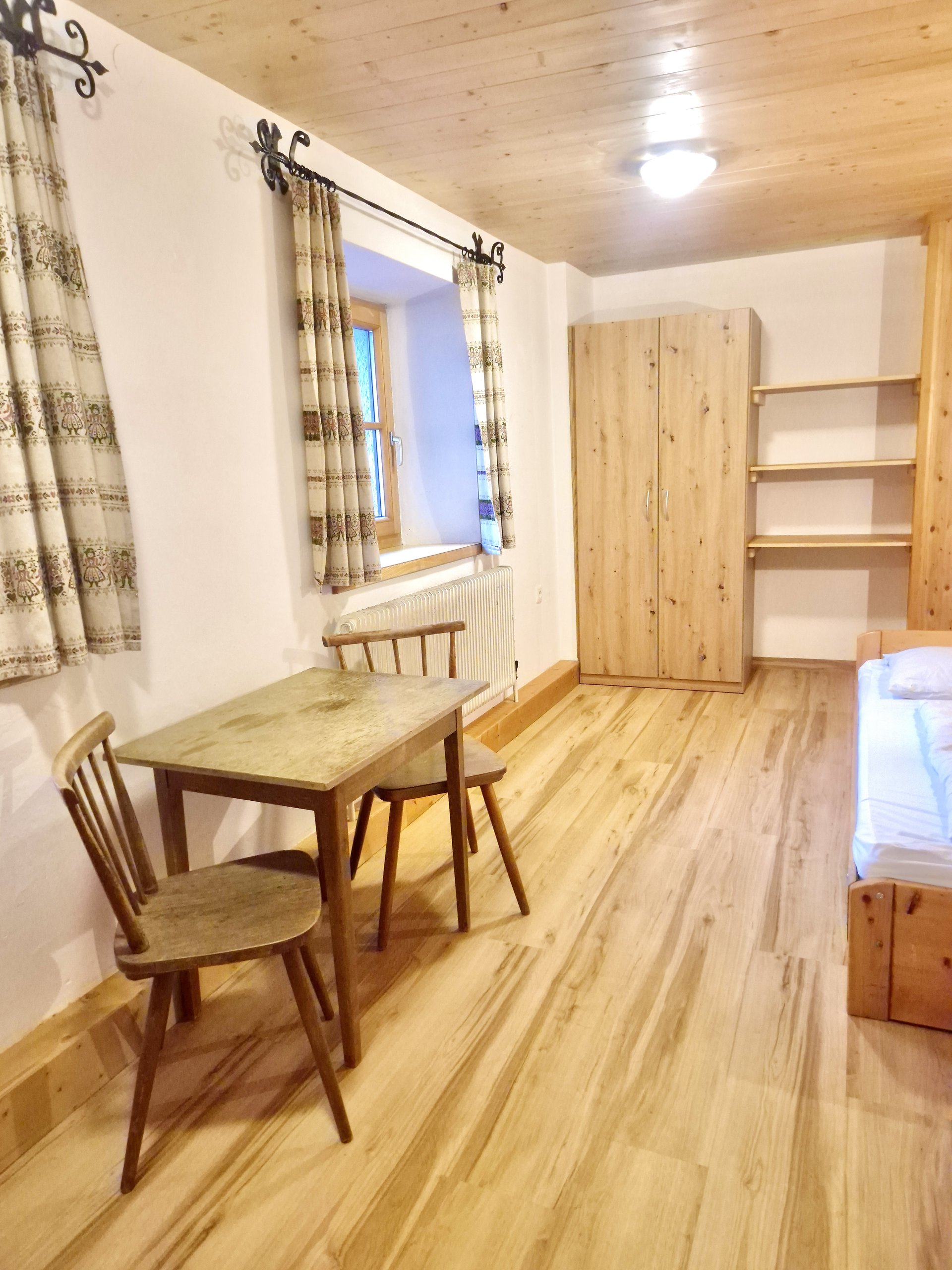 Zimmer im Selbstversorgerhaus Stuhlfelden mit Holzboden, Tisch, zwei Stühlen, Kleiderschrank und Fenster