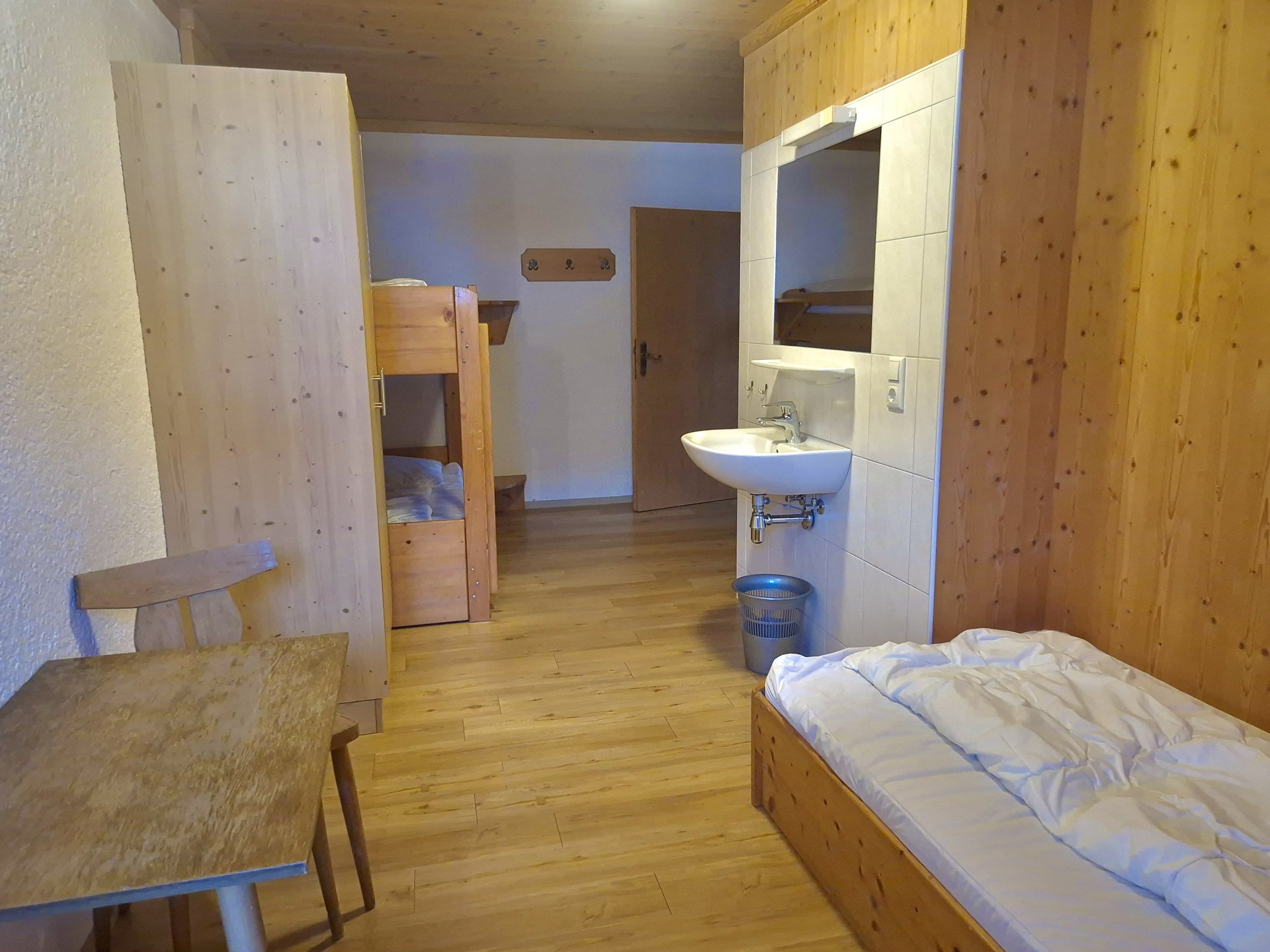 Dreibettzimmer mit Stockbett, Einzelbett, Tisch und Waschbecken im Selbstversorgerhaus Stuhlfelden